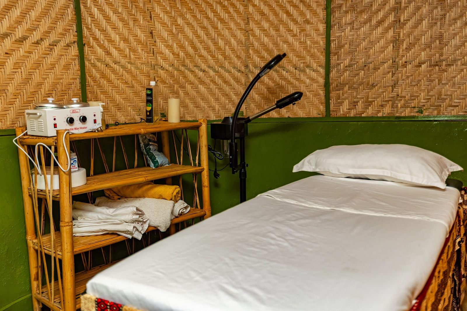Massage room with a padded treatment bed, folded towels and bamboo shelves