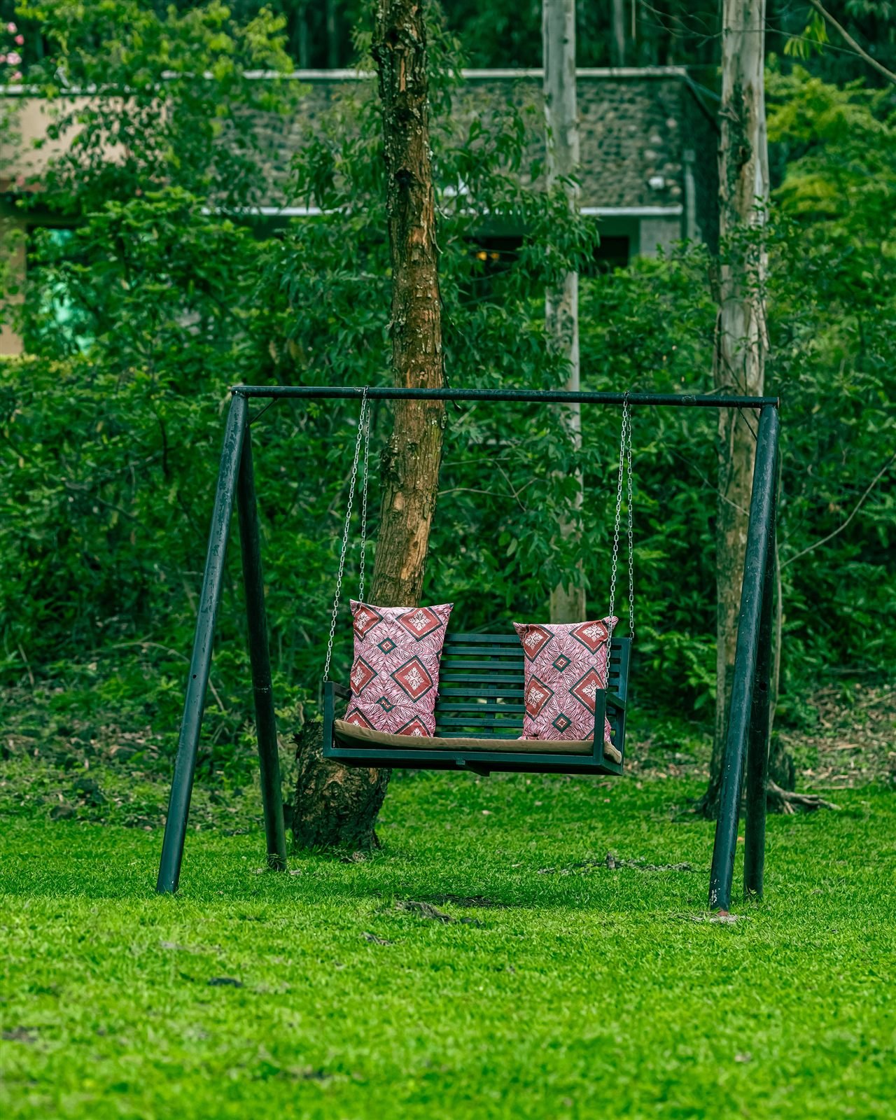 Garden swing with pink cushions under the trees